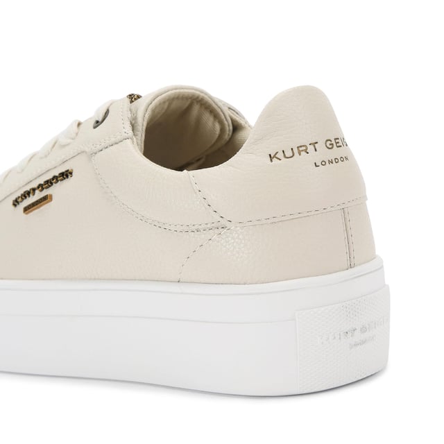 This Kurt Geiger Greenwich Cupsole sneaker features a grained taupe leather upper. The front laces up with antiqued brass branding across the upper.