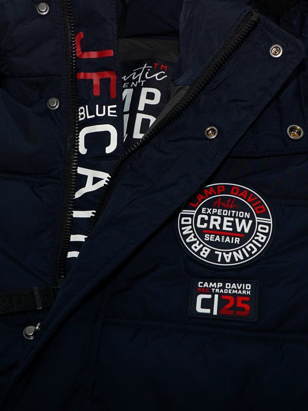 Diese Steppjacke für Herren ist ideal für kältere Tage. Es hat eine reguläre Passform, die genügend Bewegungsfreiheit und hohen Tragekomfort bietet. Die Jacke verfügt über einen hohen Stehkragen und eine zusätzliche, separat mit Druckknöpfen verschließbare Kapuze – der optimale Schutz vor Wind und Kälte. Die Jacke selbst wird mit einem verdeckten Reißverschluss geschlossen. In den beiden Seitentaschen können Essentials verstaut werden. Diverse Label-Details runden das Design ab.