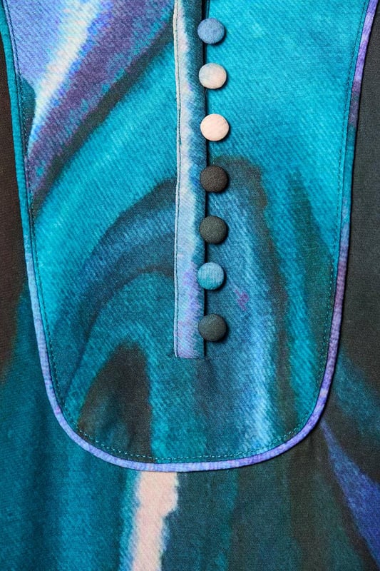 Stijlvolle damesjurk met verfijnde details en unieke printDe Dhalia Print Jurk is een schitterend en elegant kledingstuk met oog voor detail. De semi-transparante stof geeft een luchtig en verfijnd effect, terwijl de voering zorgt voor comfort en ondoorzichtigheid tijdens het dragen. De olieachtige print straalt in diverse kleuren, waaronder paars, aquagroen en een zwarte achtergrond, wat een eigentijdse en trendy uitstraling toevoegt. De prachtig uitgewerkte details, zoals het opstaande kraagje met plastron en bedekte knoopjes, de pofmouwen met manchetten en dezelfde verfijnde knoopjes, evenals de luxe plooien en piping bij de schoudernaden en rugpas, dragen bij aan de geraffineerdheid van het ontwerp. De jurk heeft een wijd uitlopende, lange blouse-stijl die zorgt voor een flatterend en elegant silhouet. De subtiele steekzakken in de zijnaden voegen een comfortabel element toe aan deze chique printjurk, waardoor de jurk zowel elegantie als functionaliteit combineert. Met zijn opvallende print, pofmouwen en prachtige details is deze jurk een veelzijdige aanvulling op elke garderobe. Op zoek naar extra warmte in de winter? Combineer de jurk met het aquagroene Parker vest voor een opvallende en stijlvolle look. Deze printjurk is absoluut een waardevolle toevoeging aan je nieuwe garderobe!"