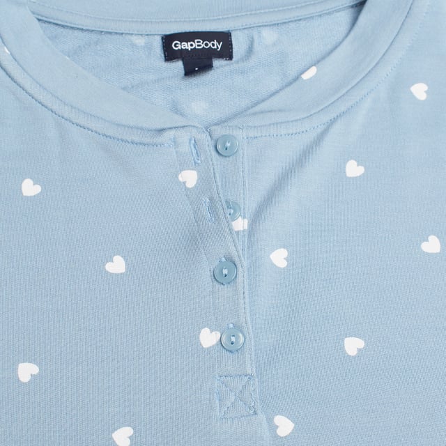 Esta camiseta de pijama de manga larga de GAP es una opción ideal para quienes buscan la combinación perfecta de comodidad y estilo durante el descanso. 

Confeccionada en un tejido suave y ligero, garantiza una sensación acogedora sobre la piel, permitiendo un sueño reparador y tranquilo.

El diseño presenta un estilo Henley clásico, con un cuello redondo y un cierre de botones, lo que no solo añade un toque elegante, sino que también permite ajustarlo según la preferencia personal, ofreciendo versatilidad y confort. 

El corte holgado y relajado asegura libertad de movimiento, haciendo de esta camiseta una prenda ideal no solo para dormir, sino también para relajarse en casa.
 Composición: 96% Modal, 4% Elastano
 Cuidados:
- Lavar a máquina con agua fría.
- Utilizar colores similares en el lavado.
- Evitar el uso de blanqueadores.
- Secar a baja temperatura en secadora.
- Planchar a baja temperatura.
- No lavar en seco.