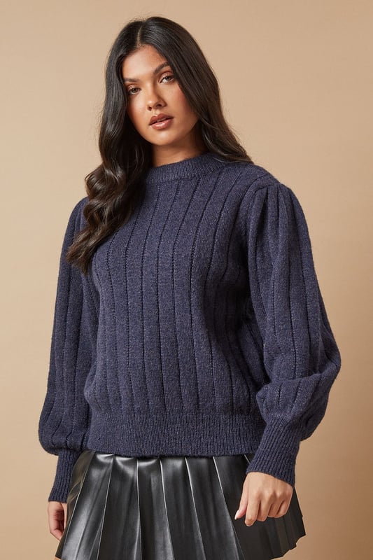 Ribbed knit texture for added visual interest
        Elegant bow detail at the back for a feminine touch
        Voluminous balloon sleeves create a striking silhouette
        Crew neckline for a classic finish
        Versatile design suitable for various casual occasions
    
    This Oasis Bow Back Ribbed Jumper effortlessly combines comfort with style, making it a must-have addition to your wardrobe. The ribbed knit texture adds depth and interest to the design, while the charming bow detail at the back introduces a delightful feminine flair. The jumper's standout feature is undoubtedly its voluminous balloon sleeves, which create a dramatic and eye-catching silhouette. For a casual yet chic ensemble, pair this jumper with a pleated leather-look skirt and knee-high boots, as shown in the image. This versatile piece is perfect for family gatherings, brunch dates, or casual outings with friends. To dress it up for evening drinks, consider swapping the boots for heeled ankle booties and adding statement earrings. The jumper's adaptable nature ensures it will become a go-to item in your wardrobe, easily transitioning from day to night with simple styling tweaks.