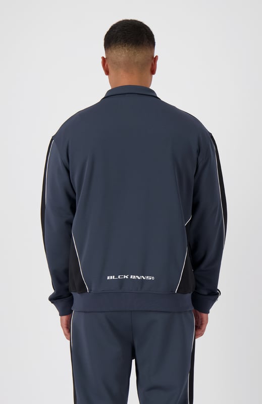 100 % Polyester Hoher Kragen mit durchgehendem Reißverschluss Schwarzes BNNS-Logo auf der Brust Zwei Reißverschluss-Fronttaschen Mit Streifen an den Ärmeln Kombinierbar mit PANEL-V1 TRACKPANTS 
