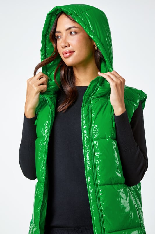 Patent Hooded Gilet from Roman. Add a pop of colour and a unique twist to your casualwear with our bold hi-shine gilet! The perfect layer for transitioning into Autumn, this cosy staple has a padded silhouette and cosy funnel neckline for warmth. With a secure zip fastening, this jacket also has drawstring detail and a glossy high shine finish. This statement jacket is a fashionable yet functional layering piece with zipped side pockets and a showerproof hood. Wear over relaxed denim and lightweight jumper for your own runway inspired outfit!