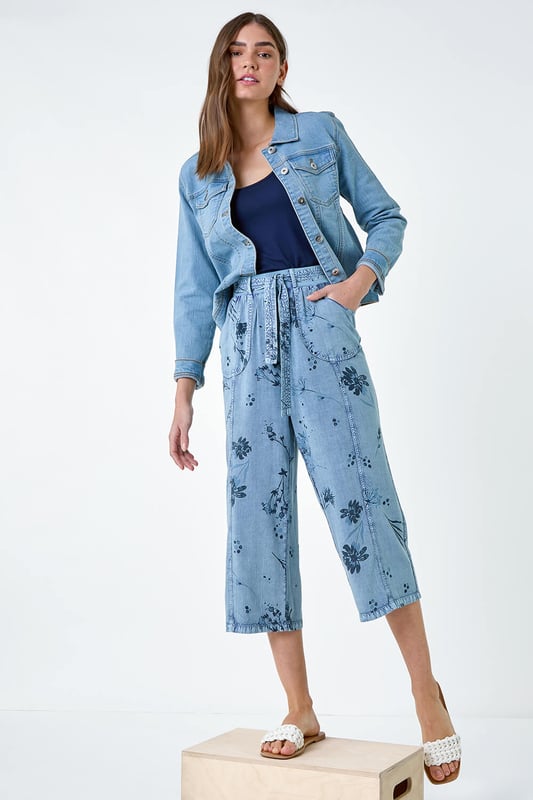 Floral Print Culotte Trousers from Roman. Add a touch of floral flair to your Spring wardrobe with these stylish culotte trousers. Featuring a cute floral print on a denim wash backdrop, these trousers are perfect for the new season. The elasticated waist with a tie belt detail offers both comfort and style, while the cropped culotte length and wide leg shape create a flattering silhouette. The light woven material and pull-on design make them a real Spring staple. Complete your look with a denim jacket, cami top and sandals for effortless daywear.