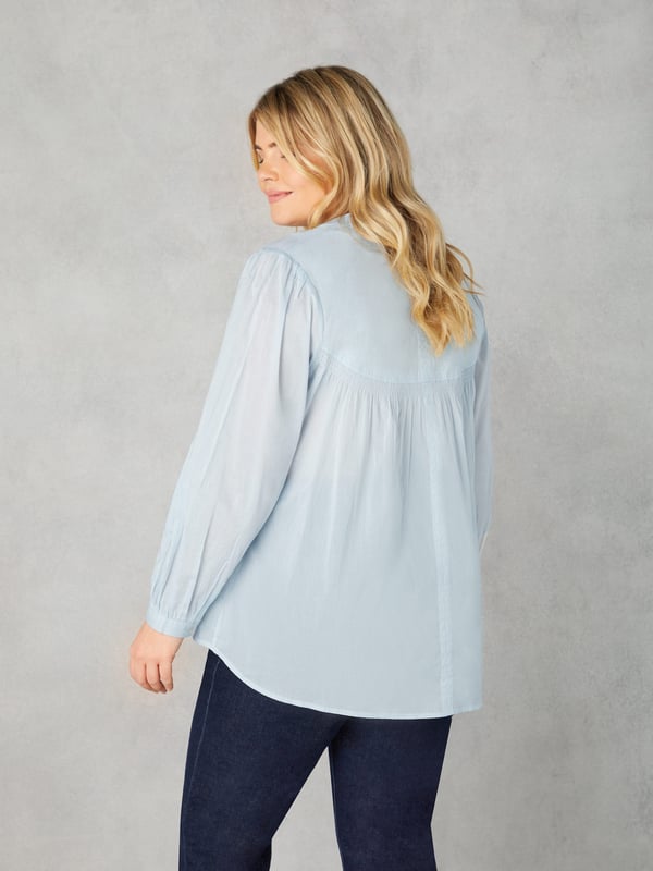 In classic blue, this blouse is cut from the softest of cottons. With a nehru collar, it has a button-up front placket with pretty rouleau buttons, as well as shirring detail at the yoke. Full-length sleeves with button up cuffs create an elegant silhouette, especially when combined with its high-low hem which provides that all-important coverage.