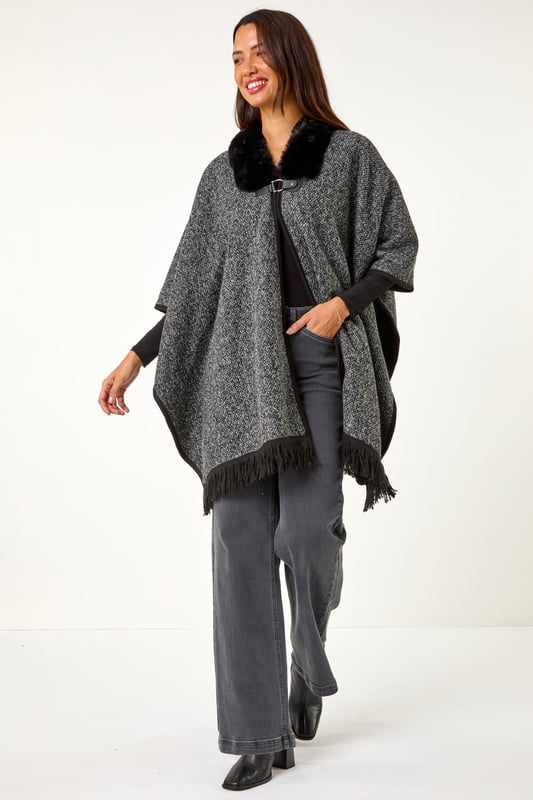 Faux Fur Fringe Hem Poncho from Roman. This style is ONE size.  Wrap up in style with this chic fringe detail poncho. Featuring a luxurious fur trim collar for added elegance and a trendy fringe hem for a playful finish, this poncho is the perfect layering piece for the Autumn/Winter season. Throw it on over your favourite knitwear and jeans for a fashion-forward look that will keep you both warm and stylish throughout the colder months!