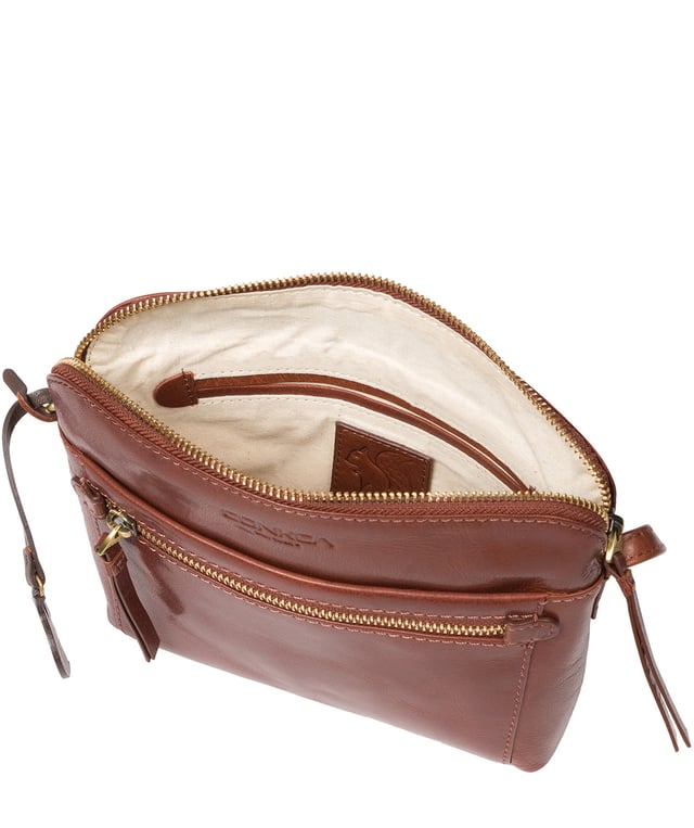 Handcrafted from natural leather, the 'Frida' cross body bag from Conkca London has a beautiful finish. A zip-over top secures a central compartment which is lined with 100% natural cotton and includes two slip pockets - ideal for a phone and keys. On-the-go storage is provided by spacious zipped pockets on the front and back of the bag alongside a slip pocket. This accessory is finished with a slim and adjustable leather strap and adorned with the inimitable Conkca squirrel logo and charm.