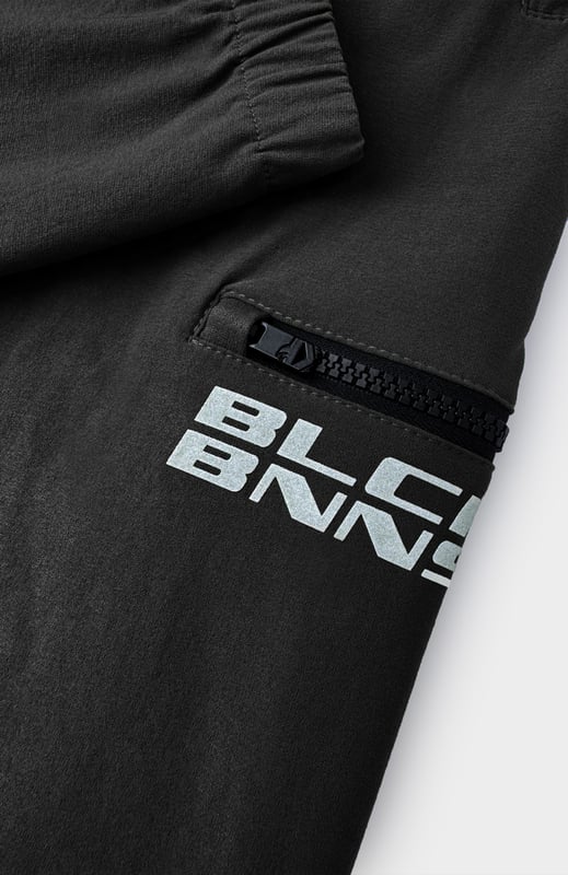 90 % Nylon | 10 % Elastan Elastischer Bund Schwarzes BNNS-Logo auf dem linken Bein Zwei Reißverschluss-Fronttaschen Kombinierbar mit INITIAL TECH JACKET 