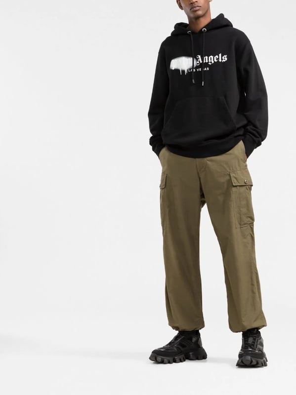Palm Angels reemplaza su logotipo cl�sico con esta versi�n de Las Vegas, realzada con un efecto de pintura en aerosol en color blanco sobre un fondo negro s�lido. Confeccionada con algod�n suave, esta selecci�n SS22 tiene un corte relajado que encarna la est�tica de la marca y se completa con un pr�ctico bolsillo canguro en el centro.