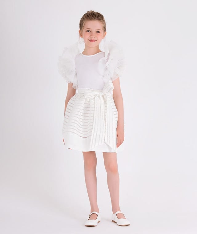 Mama Luma's sophisticated portfolio takes inspiration from a bygone era. This girls white strap skirt is both captivating and beautifully constructed. Crafted in a polka-dot bobbled effect via a chiffon effect on a peplum hem. It is complete with a tie-up bow and satin stripe trim. She will embody unparalleled confidence.  Mesh/Cotton Lining  100% Polyester