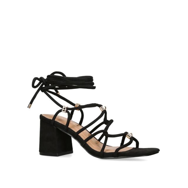 The KG Kurt Geiger Raya heel features a black microsuede upper with gold and KG Kurt Geiger stud hoops connecting the straps. The heel is a classic high block style. Heel height: 70mm.
