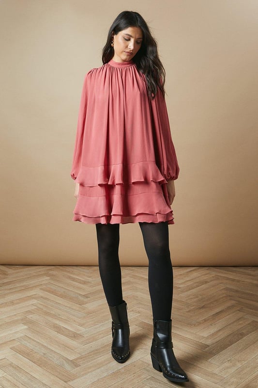 Elegant high neck design for a sophisticated look
        Flowy chiffon fabric creates a graceful silhouette
        Voluminous balloon sleeves add a romantic touch
        Tiered ruffle hem for playful movement
        Versatile mini length suitable for various occasions
    
    This charming high neck chiffon mini dress from Oasis is the epitome of feminine allure. The airy chiffon fabric drapes beautifully, creating a flattering and comfortable fit for all-day wear. The dress features eye-catching balloon sleeves that add a touch of drama to your ensemble, while the tiered ruffle hem introduces a playful element to the overall design. Perfect for casual daytime events, this dress can be styled effortlessly for family gatherings or weekend brunches. Pair it with ankle boots and a leather jacket for an edgy contrast, or opt for ballet flats and delicate jewellery for a softer look. The versatile nature of this dress allows for easy transition from day to night - simply swap your accessories to suit the occasion. Embrace your girly side and make a statement in this delightful Oasis creation.