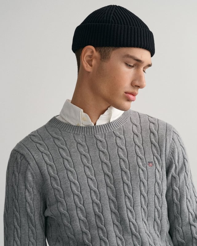 This GANT men's sweater in a traditional cable knit pattern is a stylish addition to any modern wardrobe. With its classic crew neck and ribbed trims, it offers a comfortable fit, while the embroidered GANT crest graphic on the chest provides a sophisticated accent. It pairs perfectly with jeans or pants.