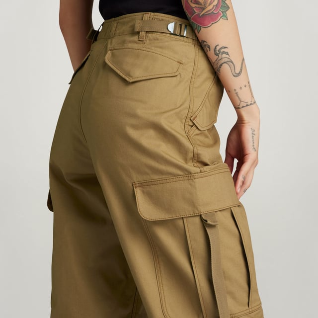 Flap pockets at the waist and back- hidden snap button. Cargo pockets at the thigh- hidden snap closure. Adjustable leg hem- Integrated tape. Zip & button closure. High waist. Cargo pants Drawcord show a straight fit with a shortened length. The straps at the back allow for a tighter waist. The pleats at the knee add more shape. The cargo pockets show an additional pull strap. 70% Cotton, 30% Cotton (Recycled). Canvas woven. Peach finish, soft touch. Straight