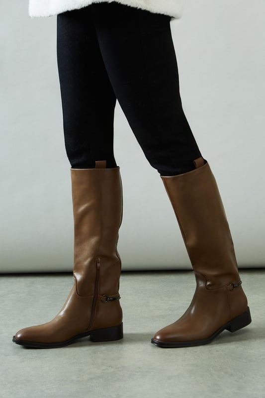 Knee-high riding boot design with sleek silhouette
        Faux leather construction for a polished look
        Distinctive stirrup detail adds equestrian flair
        Low heel measuring between 5 and 6.5cm for comfortable wear
        Side zip closure for easy on and off
    
    Step into sophistication with the Keely Faux Leather Stirrup Detail Low Heel Riding Knee Boot from Wallis. These elegant boots manifest a perfect blend of style and practicality, ideal for the woman who values both comfort and glamour. The knee-high silhouette elongates the leg, while the low heel ensures all-day wearability. Style these versatile boots with skinny jeans and an oversized jumper for a chic daytime look, or pair them with a flowing midi dress for family gatherings. The stirrup detail adds a touch of equestrian charm, making these boots a standout choice for casual outings or countryside walks. Whether you're running errands or meeting friends for brunch, these boots will keep you looking effortlessly stylish and feeling comfortable throughout your day.