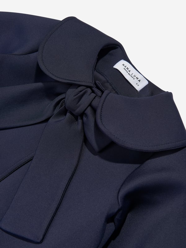 Mama Luma incorporate beautiful eco-friendly materials into their sophisticated handmade constructions. This girls navy long coat is reflective of the Californian label's precision of beauty. It showcases a Peter Pan collar, tie-up bow and balloon sleeves.  Cuffs Cotton Lining