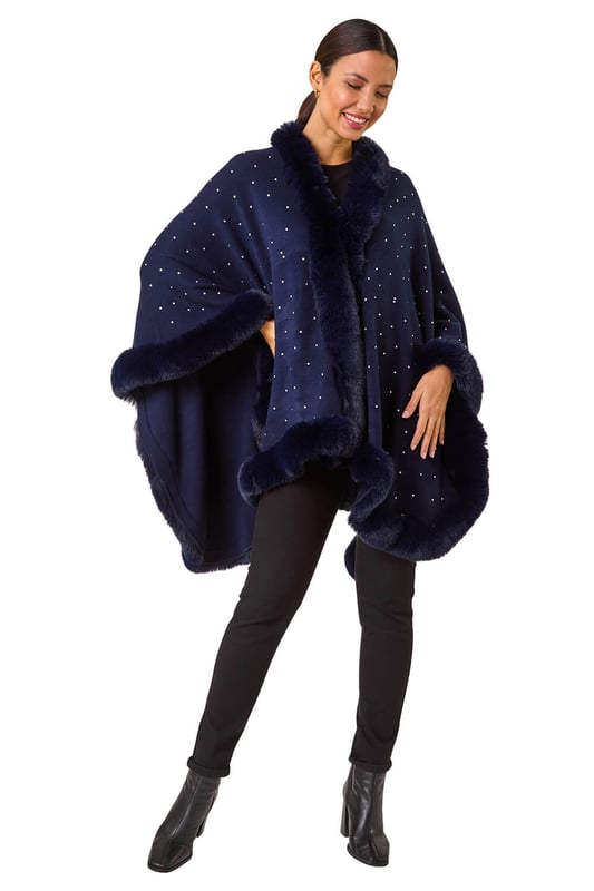 Hotfix Faux Fur Trim Cape from Roman. This style is ONE size.  Wrap up in style this Autumn and Winter with this all over hotfix faux fur trim cape. In a classic black hue with dazzling silver hotfix detailing, this cosy cape is the perfect layering piece. Simply throw on over a t-shirt and jeans for an effortlessly chic and stylish look.