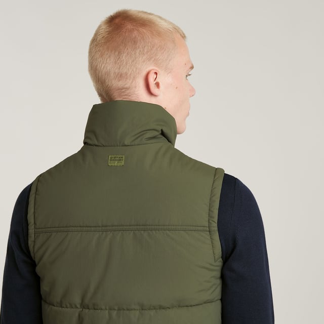 Raised collar. Sleeveless. Straight hem. Flap pockets at the chest, side pockets- hidden snap button closure. Inner pocket and hanger loop. Concealed zipper closure, snap buttons. Zip & snap closure. Densely woven fabric, enriched with a PFC free water repellent finish. Vest Foundation is padded and stitched through horizontally. Pockets are created at the chest as well as the sides. The zipper closure is covered by a wind blocker with snap buttons. Inside, an additional pocket is created to complete this sleeveless padded jacket. Densely woven. Compact woven. Coated with a high performance water repellent finish for optimal functionality.