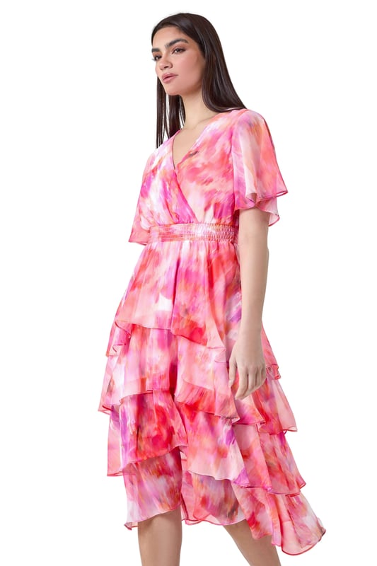 Abstract Print Chiffon Tiered Midi Dress from Roman. Discover pure elegance with this abstract print tiered midi dress from the Ariella collection. This wedding guest staple features a soft chiffon fabric with a flattering tiered silhouette and a v-neckline. Designed with a wrap front and shirred stretch waist for a fit and flare shape, this will be flattering for any formal event. The vibrant abstract print, split detail skirt, and short floaty sleeves add a touch of femininity to the finished look. Whether you're ready for a day at the races or you're Mother of the Bride, this dress is easy to pull on overhead and style with heels for timeless occasionwear.
