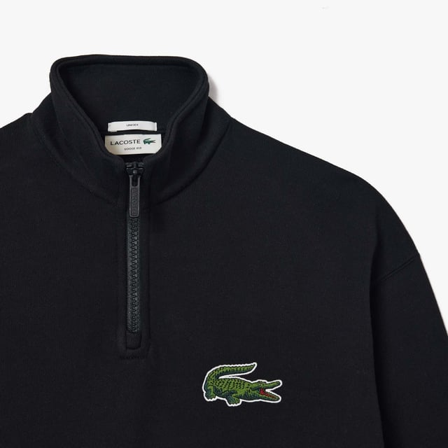 Unisex Lacoste Loose Fit High Neck Sweatshirt in Black. Finest materials, brand’s singular expertise. The perfect expression of Lacoste’s timeless wardrobe.- Loose fit is loose ease on body and sleeves, lower shoulders and armholes.- Half zipped sweatshirt in organic heavy French terry with big croc 80' on chest.- Unisexe.- Zipped high collar in shell fabric.- 7cm iconic original badge crocodile.- 3cm green crocodile at under middle back collar. Material: 100% Organic Cotton. Ref: SH0069031.