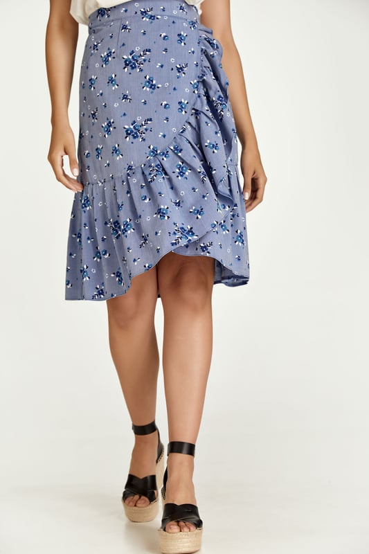 Esta falda cruzada floral está confeccionada en tejido de viscosa estilo denim. La falda se abrocha con una corbata de 4,5 cm del mismo tejido que pasa a través de un agujero en la costura lateral, justo debajo de la cintura. La falda tiene un ribete de volantes de 26 cm por todas partes. Tiene un estilo sutil con una silueta de línea A y llega hasta la rodilla.