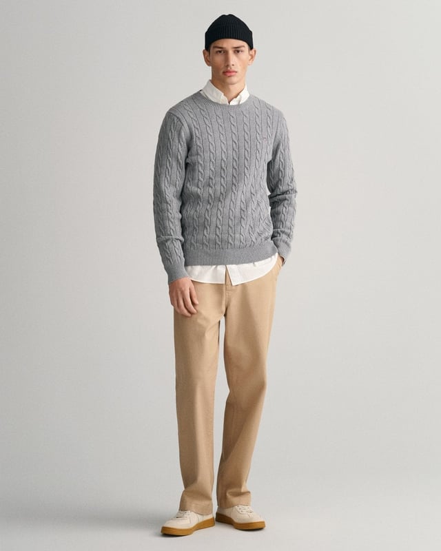 This GANT men's sweater in a traditional cable knit pattern is a stylish addition to any modern wardrobe. With its classic crew neck and ribbed trims, it offers a comfortable fit, while the embroidered GANT crest graphic on the chest provides a sophisticated accent. It pairs perfectly with jeans or pants.