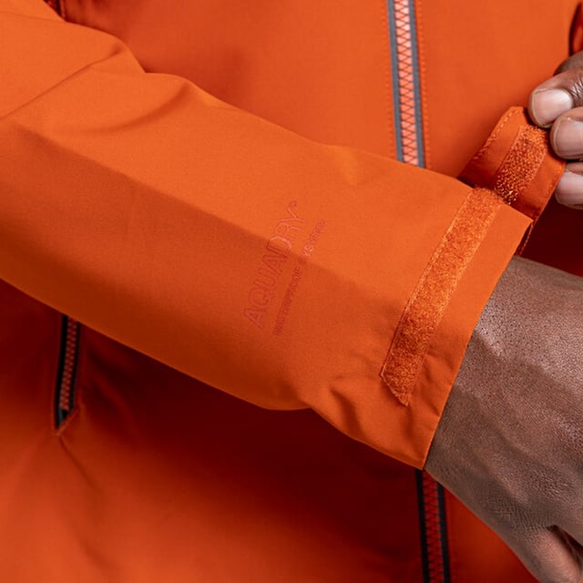 Materialzusammensetzung (%): 100% Polyester. Design: Logo, Unifarben. Gewebetechnik: Aqua Dry, Atmungsaktiv, Wasserfest, windbeständig. Hoch geschnitten. Bündchen: Klettverschlussriemen. Langärmlig. Reflektierende Details. Kapuzenmerkmale: Knebel-Einstellung. Taschen: 3. Wasserdichter Reißverschluss. Atmungsaktivitätsbewertung: 15000. Wasserdichtigkeit (mm): 8000 mm. Nachhaltigkeit: Aus recyceltem Material.