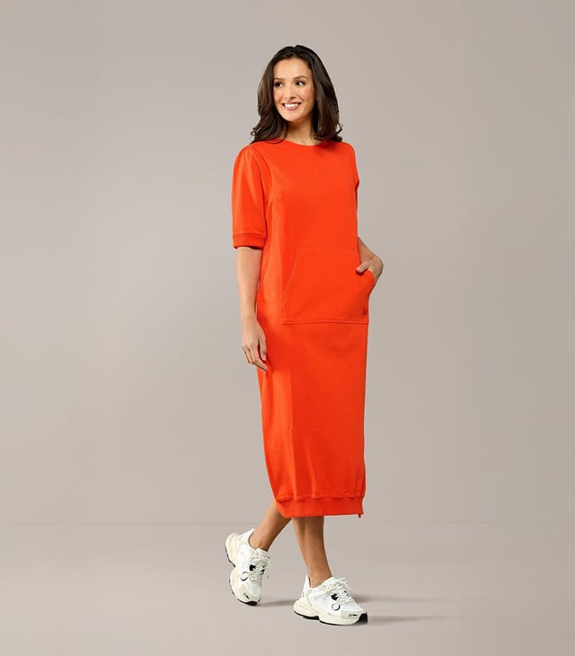 Ervaar de perfecte balans tussen stijl en comfort met deze prachtige lange sweaterjurk in een levendige oranje tint, een absolute must-have uit de collectie van Caroline Tensen. Dit veelzijdige kledingstuk combineert moeiteloos elegantie met ultiem draagcomfort. Gemaakt van 100% katoen, voelt de zachte sweaterstof heerlijk aan op de huid en biedt het een comfortabele pasvorm die je het liefst de hele dag draagt. De jurk is voorzien van subtiele pofmouwen en ribboorden bij de mouwen, kraag en zoom, wat zorgt voor een speelse en charmante uitstraling. Een extra praktisch en stijlvol detail is de kangoeroezak met verfijnd borduurwerk. Op de rug bevindt zich bovendien een uniek borduursel, geïnspireerd door de persoonlijke tatoeage van Caroline Tensen. Met zijn lange, vloeiende pasvorm en opvallende oranje kleur geeft deze jurk een frisse en vrolijke touch aan elke outfit. Of je nu geniet van een ontspannen dag thuis, een wandeling maakt in het park of een casual uitje hebt gepland, deze sweaterjurk is de perfecte keuze. Verrijk je garderobe met dit veelzijdige item en geniet van een ongeëvenaarde mix van stijl en comfort!