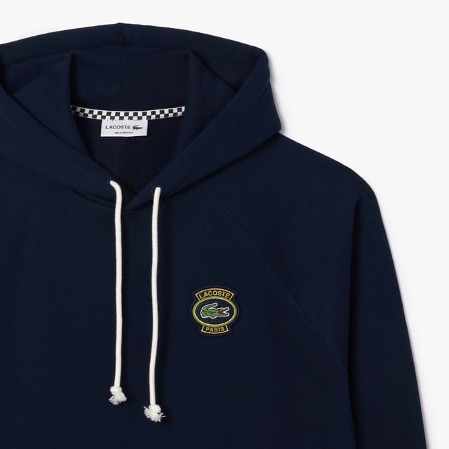 Own the french fashion sport Hoodie in French Terry Raglan sleeves Kagaroo pocket Knot drawcord 55x53 cm felt badge with Lacoste Paris embroidery and green crocodile on chest.