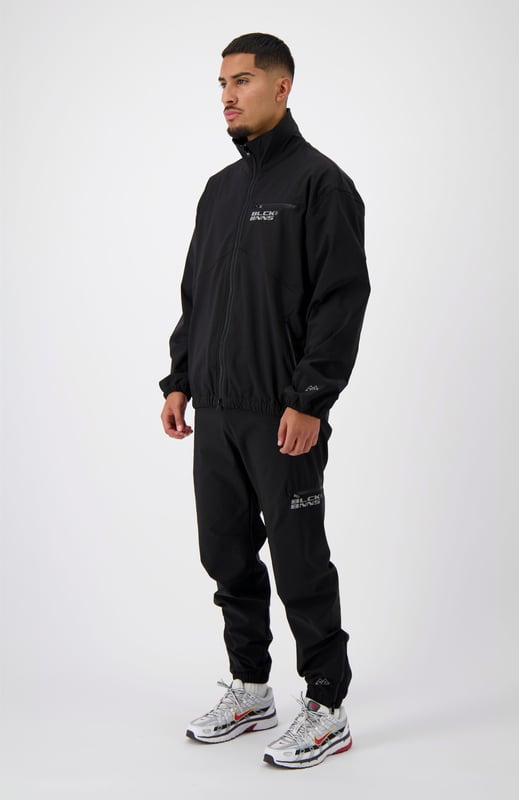 90 % Nylon | 10 % Elastan Elastischer Bund Schwarzes BNNS-Logo auf dem linken Bein Zwei Reißverschluss-Fronttaschen Kombinierbar mit INITIAL TECH JACKET 