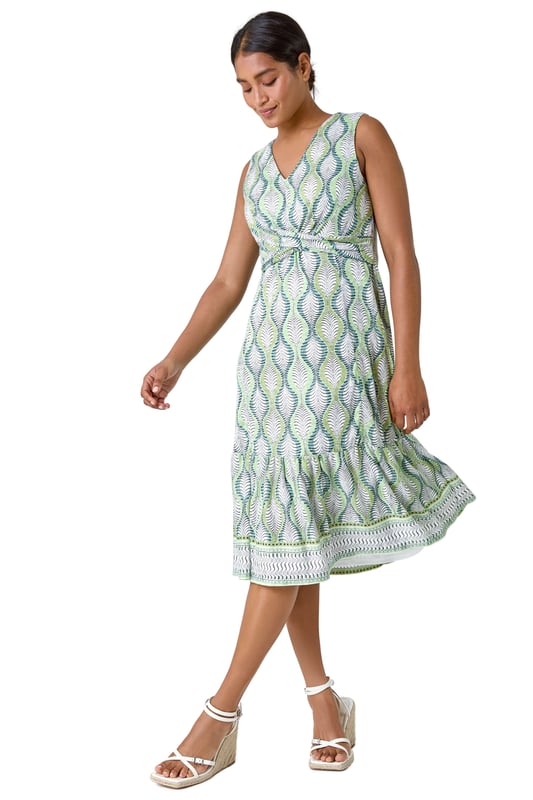 Twist Front Leaf Print Stretch Dress from Roman. Add a touch of nature to your Spring wardrobe with this stunning twist front dress. The abstract leaf print creates a fresh and playful feel, perfect for the season. The sleeveless design and v-neckline offer a feminine touch, while the knot detail at the waist flatters your figure. With its frill hem, stretch jersey fabric and burnout border print, it ensures all-day comfort and a flattering fit. Pair this midi dress with a casual denim jacket for an effortlessly chic day ensemble.