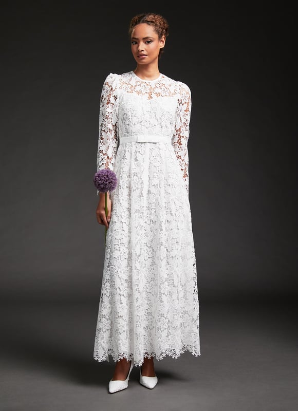 A wedding dress with a feminine, Fifties' feel, our Lola bridal dress is in our first-ever Bridal Collection. Crafted from a classic floral lace in off-white, it has a round neck, delicate puff shoulders, long sleeves, a slip layer, a nipped waist with a pretty grosgrain ribbon and a full skirt falling to just above the ankle. Every LK Bennett wedding dress arrives carefully-packaged with its own garment bag and white satin hanger, to keep it  perfectly pristine for the big day.