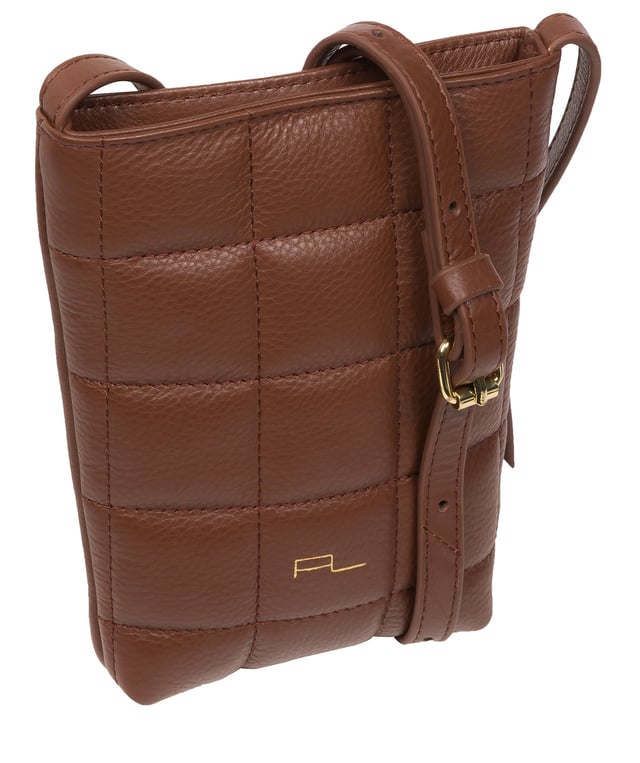 The 'Elouise' cross body phone bag from the Pure Luxuries Marylebone collection is handcrafted from high-quality, genuine Nappa leather with a natural super-soft touch. The eye-catching quilted design on the front gives the bag a unique silhouette, along with extra protection. A concealed magnetic closure keeps the contents of the bag secure. The interior is lined with 100% cotton and includes a slip pocket and two card slots. Comes with a matching and adjustable slim leather strap with a maximum drop length of 65cm. The minimalist Pure Luxuries logo is embossed in gold foil for a beautifully simple finishing touch.