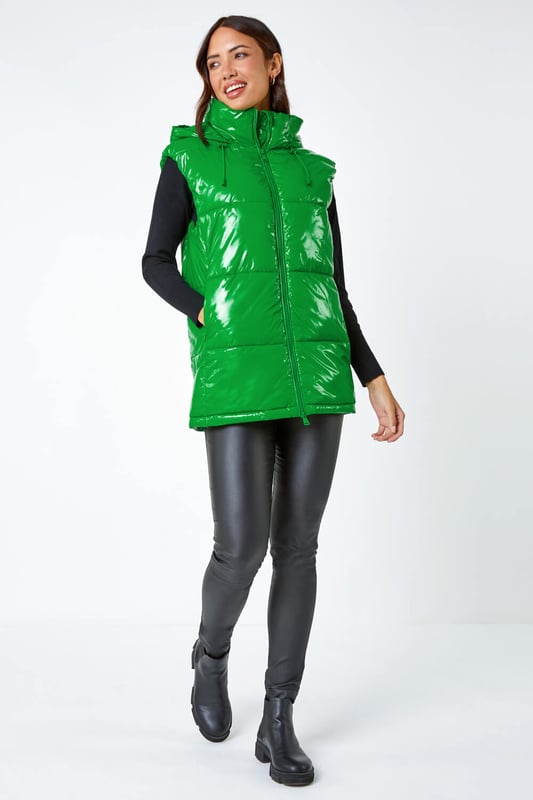 Patent Hooded Gilet from Roman. Add a pop of colour and a unique twist to your casualwear with our bold hi-shine gilet! The perfect layer for transitioning into Autumn, this cosy staple has a padded silhouette and cosy funnel neckline for warmth. With a secure zip fastening, this jacket also has drawstring detail and a glossy high shine finish. This statement jacket is a fashionable yet functional layering piece with zipped side pockets and a showerproof hood. Wear over relaxed denim and lightweight jumper for your own runway inspired outfit!