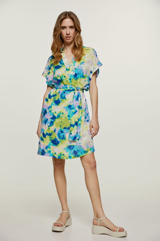 Deze zomerjurk met print is gemaakt van geweven viscose. Het is mouwloos en heeft een boord bij de armsgaten in dezelfde stof. Het heeft een mandarijnkraag van 2 cm en een sluiting van 4 cm bij de halslijn aan de voorkant om een V-vorm te creëren. Aan elke kant zit een binnenzak.  De jurk heeft grote splitten van 20 cm aan elke kant. De jurk kan worden gedragen met de riem of zonder als u een meer ontspannen zakjurkstijl wilt creëren. De riem in dezelfde stof is inbegrepen. Dit kledingstuk is gestileerd in een recht los silhouet.
