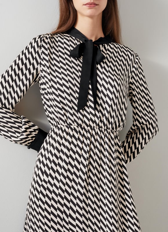 Effortless sophistication with the Bridget graphic print dress in timeless black. This smart casual piece, crafted from high-quality viscose, features a geometric design, adjustable neck tie, and convenient pull-on style. Perfectly pairs with sleek boots or classic heels for a refined look.