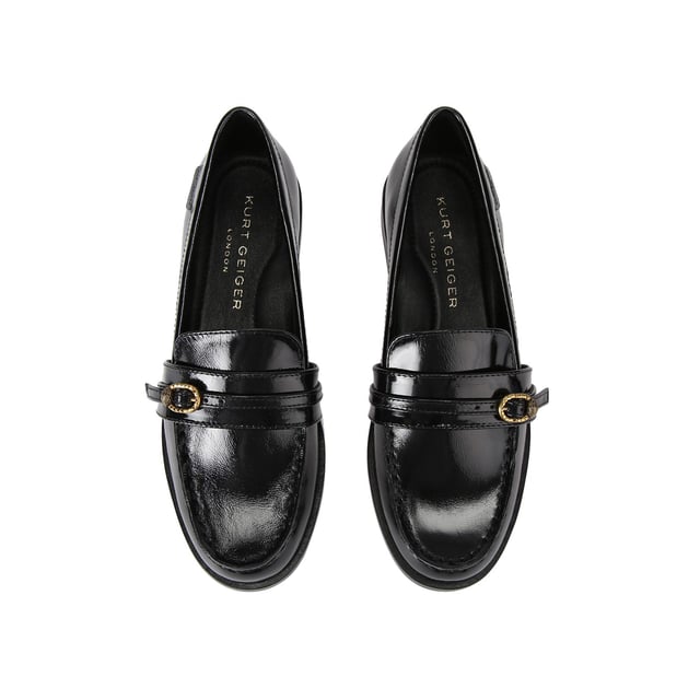 The Kurt Geiger Mayfair Slim Loafer features a black patent upper with a thin strap across the toe. There is an antiqued brass buckle with micro eagle head surrounded by crystals fastening the strap.