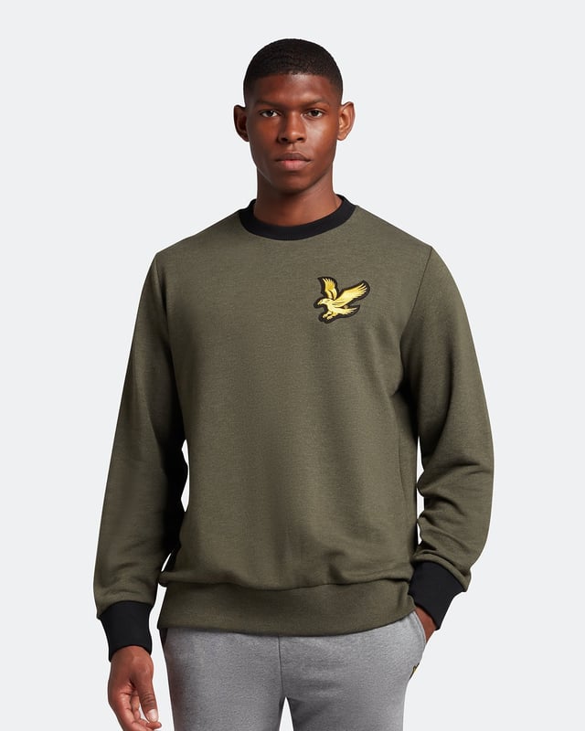 Suéter verde con logo de águila grande de Lyle & Scott. Manténgase cómodo y con estilo con el jersey Lyle & Scott Branded. Este jersey se ajusta a la talla real y presenta el logotipo de la marca Lyle & Scott. ¡Hacer una declaración nunca se vio ni se sintió tan bien! Dobladillo y puños elásticos, jersey de cuello redondo, suéter verde Lyle & Scott. 64% algodón, 36% poliéster, logotipo de la marca en el lado izquierdo del pecho. Ajuste regular, se ajusta a la talla real. Código de estilo: ML1727V W814