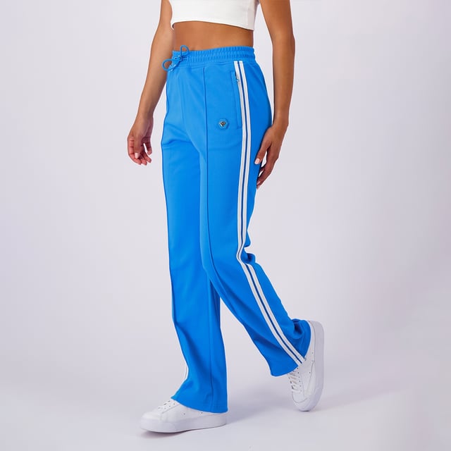 100 % Polyester, ausgestellte Passform, elastischer Bund mit Kordelzug, Reißverschlusstaschen, ikonischer Hexenaufnäher am linken Bein, sportliche Streifen an den Seiten