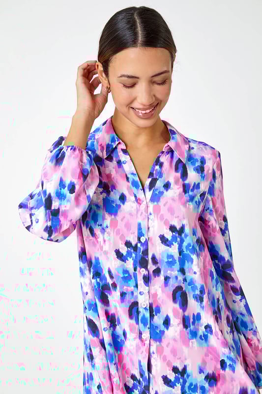 Abstract Print Dropped Hem Blouse from Roman. This sophisticated dropped hem blouse is cut from a smooth woven fabric and adorned in a colourful abstract print. It features a fully open front complete with button fastenings, full length cuffed sleeves and a smart collared neckline. A flattering dropped hem provides extra coverage at the back. Pair with cropped stretch trousers and heels for an evening out or add smart trousers and courts for work wear chic!