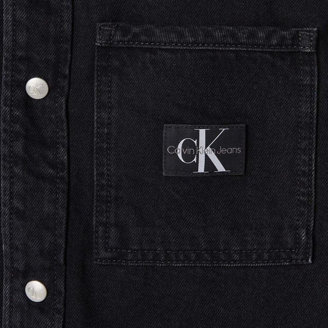 Mens Calvin Klein Logo Patch Denim Shirt in black.- Classic collar.- Front press-stud fastening.- Two chest flap pockets.- Press-stud fastening cuffs.- Faded effect.- Curved hem.- Ref: J30J3258951BY