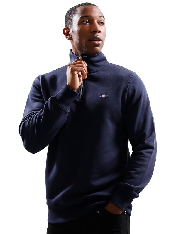 This versatile half-zip sweatshirt combines comfort and style with a premium cotton-polyester blend that's perfect for transitional weather. Featuring a small, intricately embroidered GANT graphic on the chest, it showcases a subtle yet elevated design. The ribbed hem and cuffs create a tailored silhouette. Designed for a regular fit, the half-zip collar adds a touch of sporty elegance, while the durable fabric ensures long-lasting wear.