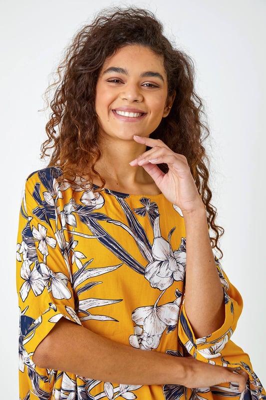 Floral Print Button Back Top from Roman. Add a light layer to your spring summer wardrobe with this short sleeve relaxed fit tee. Cut from a soft on the skin fabric, this boxy fit top is perfect for throwing on over your casual looks this season. Our large floral print top is finished with fabric covered buttons all down the back for added interest. Opt for white cropped trousers and sandals for your holiday ready ensembles.