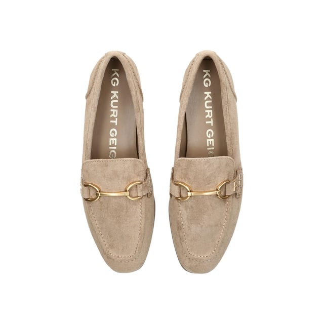 The KG Kurt Geiger Madeline is a taupe microsuede slip on loafer. There is an antiqued brass horse bit chain across the toe and small KG Kurt Geiger stud.