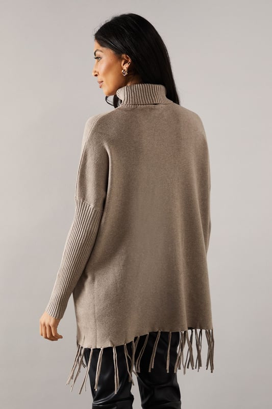Chic fringed hem poncho design for effortless style
        Cosy roll neck for added warmth and sophistication
        Relaxed fit with dropped shoulders for comfortable wear
        Ribbed cuffs and hem for a polished finish
        Versatile knitted fabric suitable for various occasions
    
    Embrace effortless elegance with this fringed hem roll neck poncho from Wallis. Perfect for the fashion-forward woman who values both style and comfort, this piece offers a sophisticated silhouette that's ideal for casual outings and family gatherings. The relaxed fit and dropped shoulders create a flattering drape, while the roll neck adds a touch of refinement. Style it with slim-fit trousers and ankle boots for a chic daytime look, or layer it over a long-sleeved top with wide-leg trousers for a more dramatic ensemble. The fringed hem adds movement and interest, making it a standout piece in your wardrobe. Whether you're running errands or meeting friends for coffee, this poncho will keep you looking stylish and feeling cosy throughout the day.