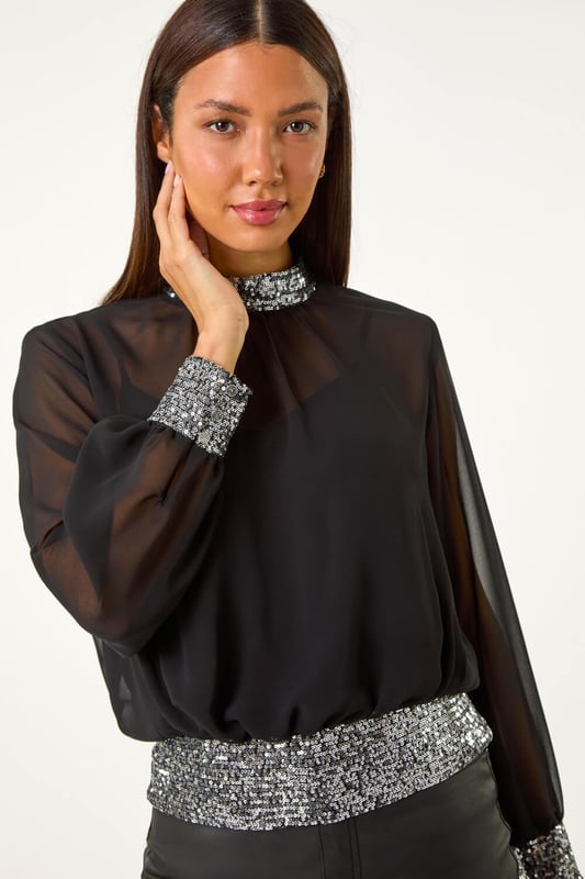 Sequin Detail Top from Roman. Shine bright in this glamourous sequin detail top, perfect for the Autumn/Winter season. Crafted from a delicate chiffon fabric, this top features intricate sequin detailing on the neck, cuffs, and hem for a touch of sparkle. The high neck and long sleeves add an elegant touch, while the included jersey cami provides coverage. Pair with tights and a skirt for a chic and festive look that will turn heads wherever you go!