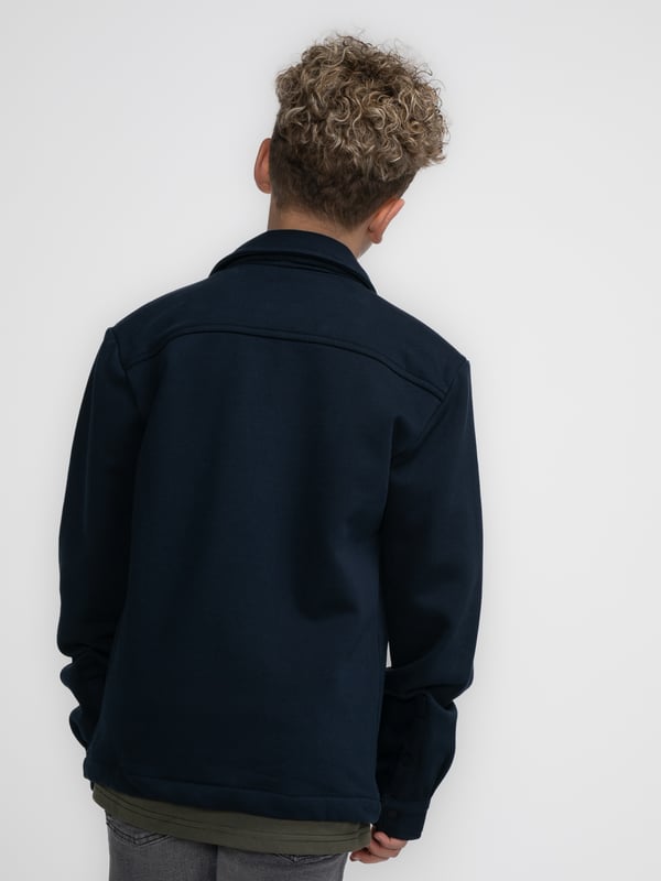 Overshirt aus Sweatstoff mit langen Ärmeln. Dieses Hemd verfügt über einen klassischen Kragen, einen Druckknopfverschluss, zwei Brusttaschen mit Druckknopfverschluss und ein Emblem auf einer Brusttasche. Das Overshirt ist mit Druckknöpfen an den Ärmeln versehen. Haben Sie Schwierigkeiten, sich zwischen zwei Größen zu entscheiden? Dann wählen Sie die größere Größe. Sweatstoff, klassischer Kragen, Druckknopfverschluss, zwei Brusttaschen, 100 % Baumwolle.