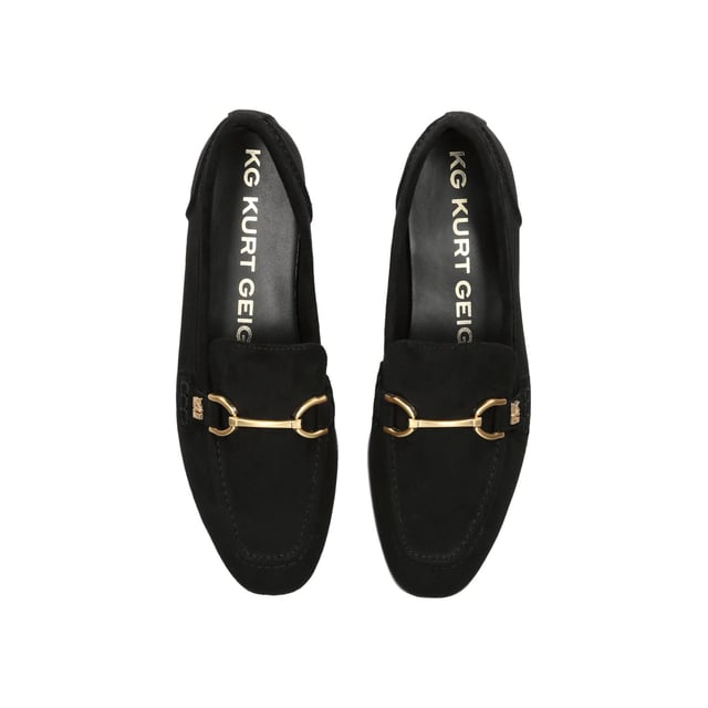 The KG Kurt Geiger Madeline is a black microsuede slip on loafer. There is an antiqued brass horse bit chain across the toe and small KG Kurt Geiger stud.