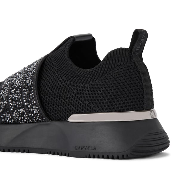 The Carvela Flare Sparkle trainer is a slip-on style with a black knitted upper. There is a crystal encrusted black fabric strap across the foot. The sole is chunky in black.