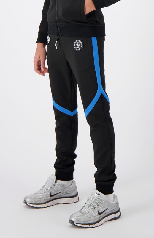 100 % Polyester Normale Passform Zwei Markenpatches auf der Vorderseite Zwei Fronttaschen Mit sportlichen Streifen verziert Kombinierbar mit JR. COMPOUND TRACKTOP 